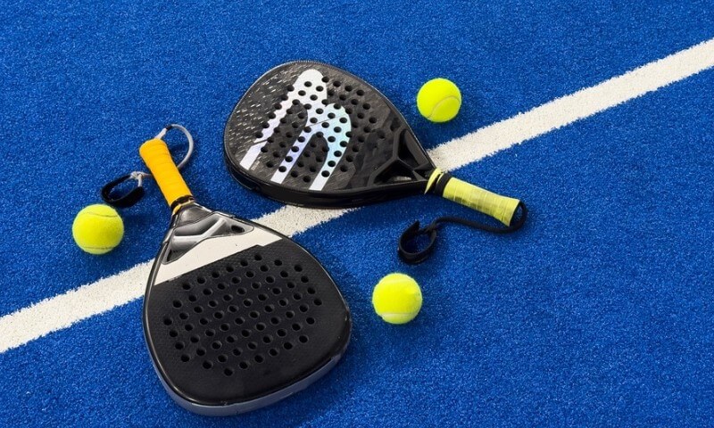 Dva teniska reketa i loptice za padel na plavom terenu